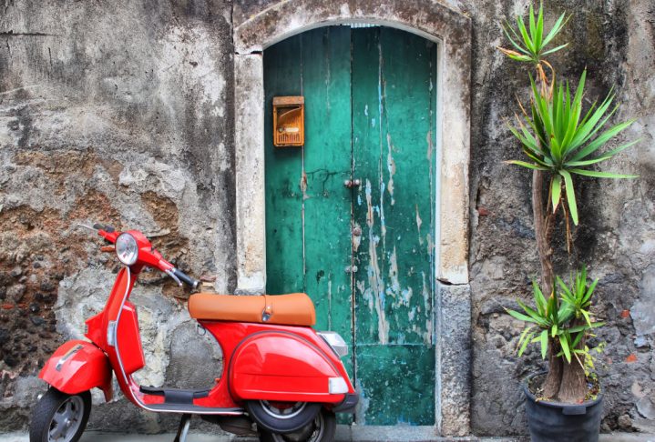 Photo of red scooter near green door and palm