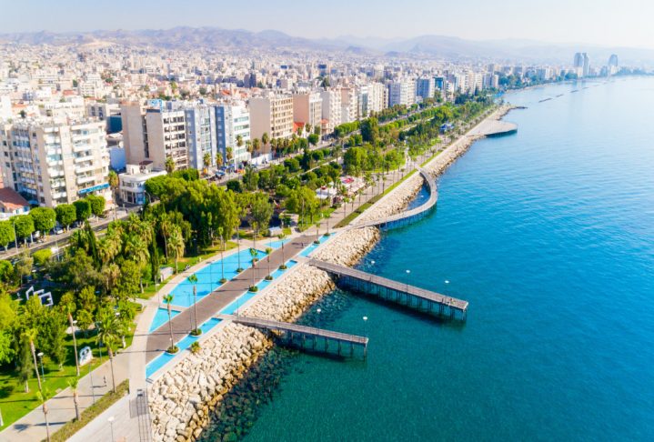 Aerial view of Molos Promenade park on the coast of Limassol city centre in Cyprus. Bird's eye view of the jetties, beachfront walk path, palm trees, Mediterranean sea, piers, rocks, urban skyline and port from above.