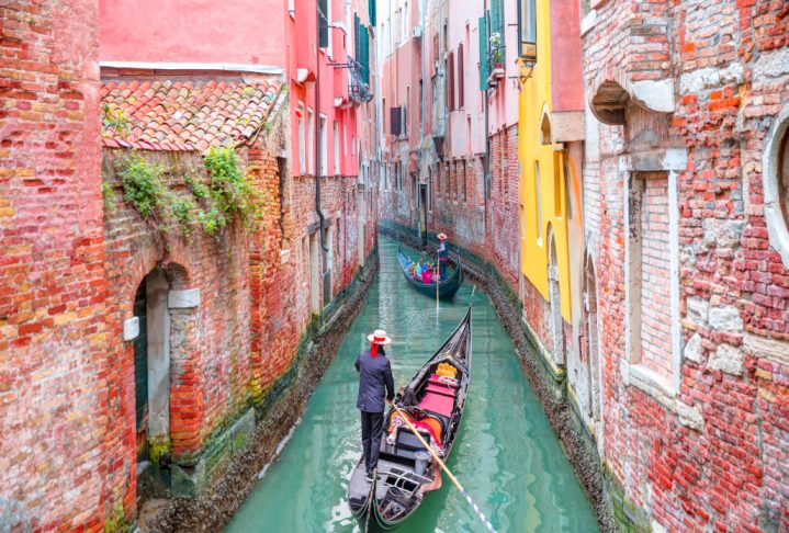 Venetian gondolier punting gondola through green canal waters of Venice Italy