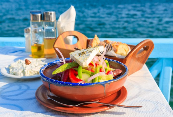 Greek salad on table in Greek tavern with blue sea water in background, Samos island, Greece