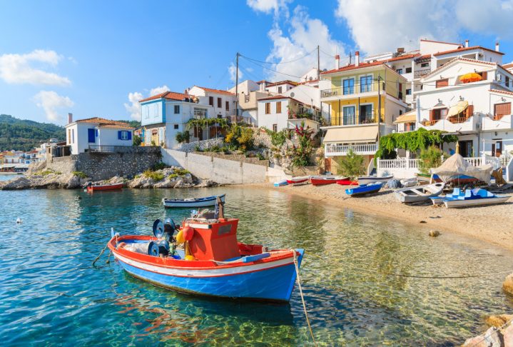 Fishing boat in Kokkari bay with colourful houses in background, Samos island, Greece